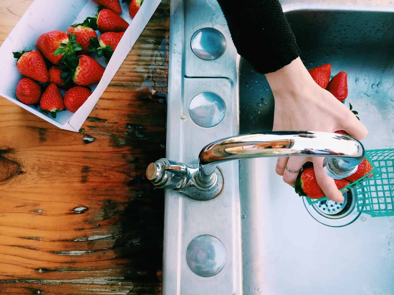 Up close of a woman's hand washing strawberries in a grey sink